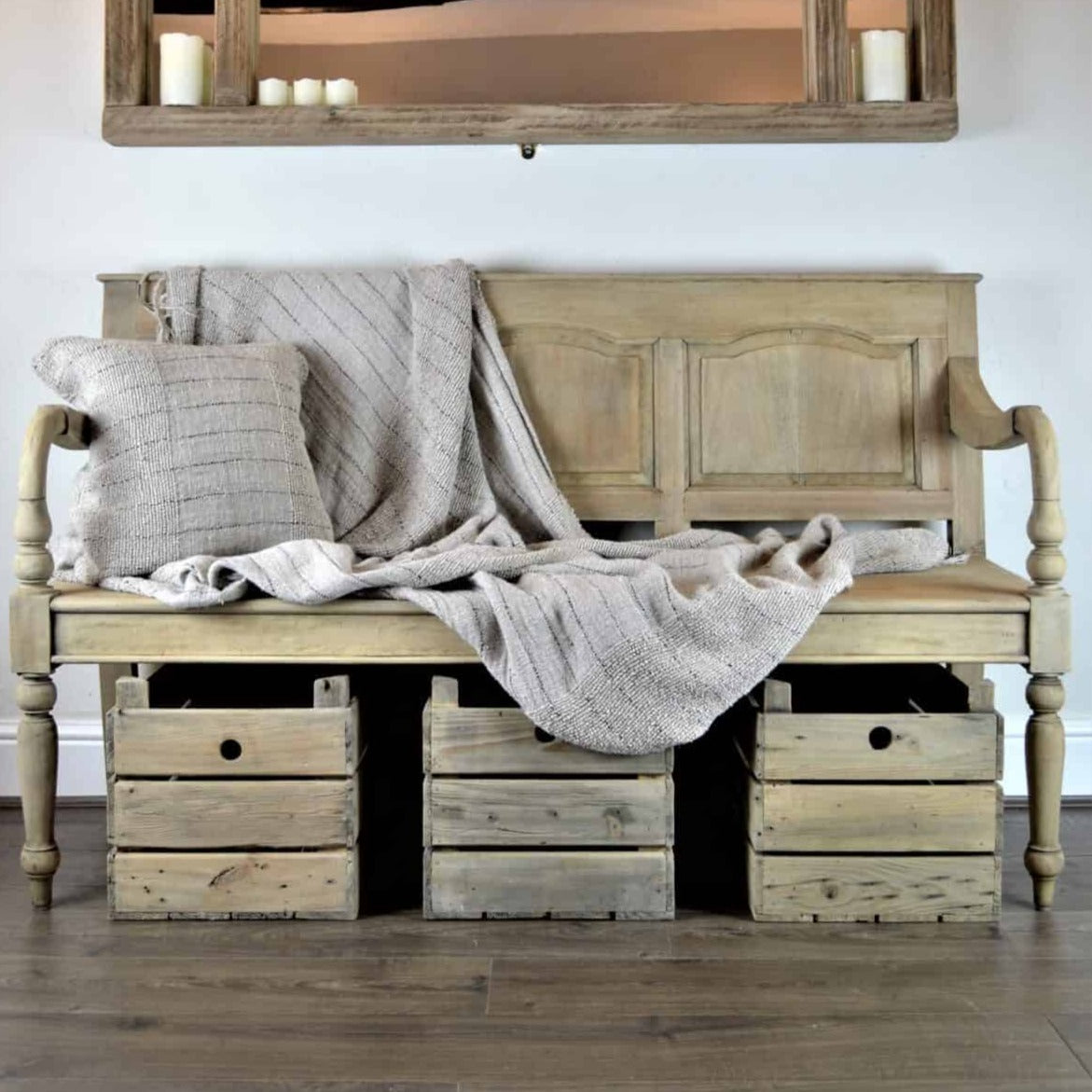 Vintage wooden bench with back with throw and cushion, and baskets underneath.