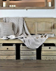 Vintage wooden bench with back with throw and cushion, and baskets underneath.