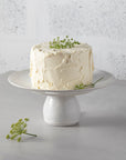 Pearly white footed cake plate with icing with white buttercream cake and green stems.