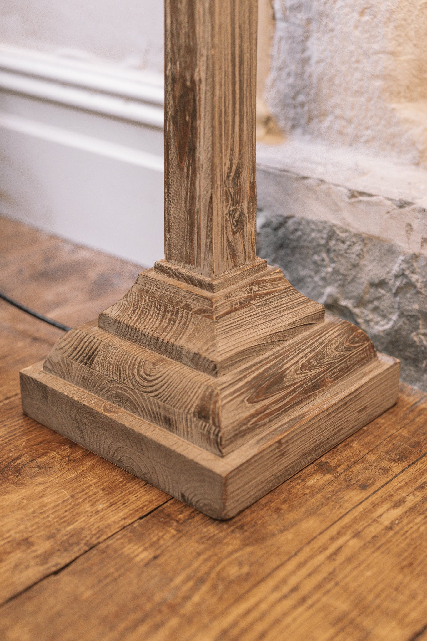 Close up of white washed wooden floor lamp base on wooden floor.