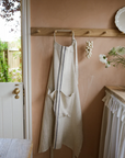 Cream and blue striped linen apron on wooden hook on wall.