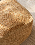 Close-up of a woven jute pouf on a wooden floor.