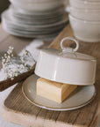 Off white butter dish with lid and loop to open on neutral wooden table with white table cloth.