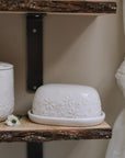Daisy Embossed Butter Dish on wooden shelf