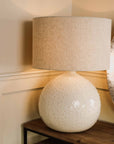 White dimpled light with linen lamp shade, switched on on wooden console.