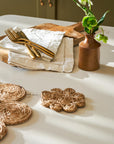 Table setting with woven jute coasters, gold cutlery, and a vase on a white surface.