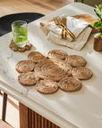 Woven jute placemats on a marble table with a glass of water and cutlery.