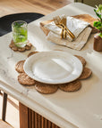 Table setting with a white plate, glass, jute placemats and cutlery on a marble surface.