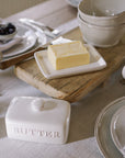 Ceramic butter dish with embossed 'butter' name, and block of butter on wooden serving board.