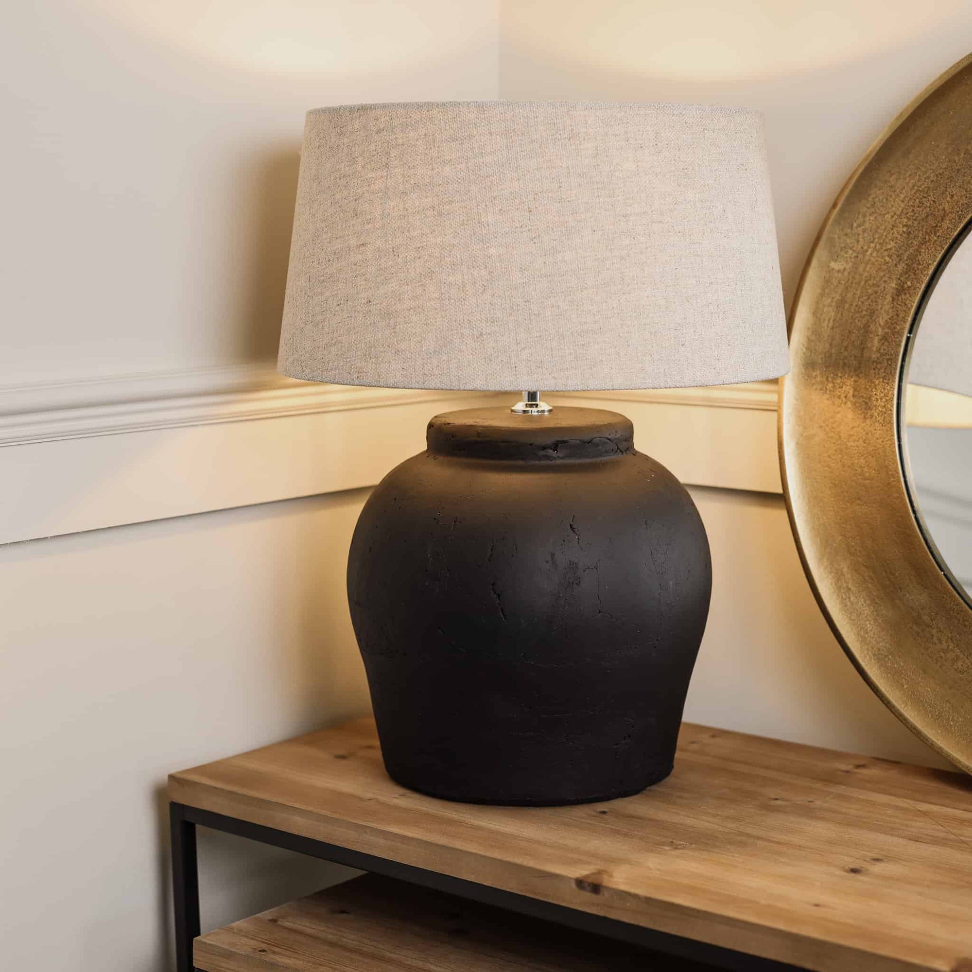 Matte black lamp with neutral shade, switched on on wooden console