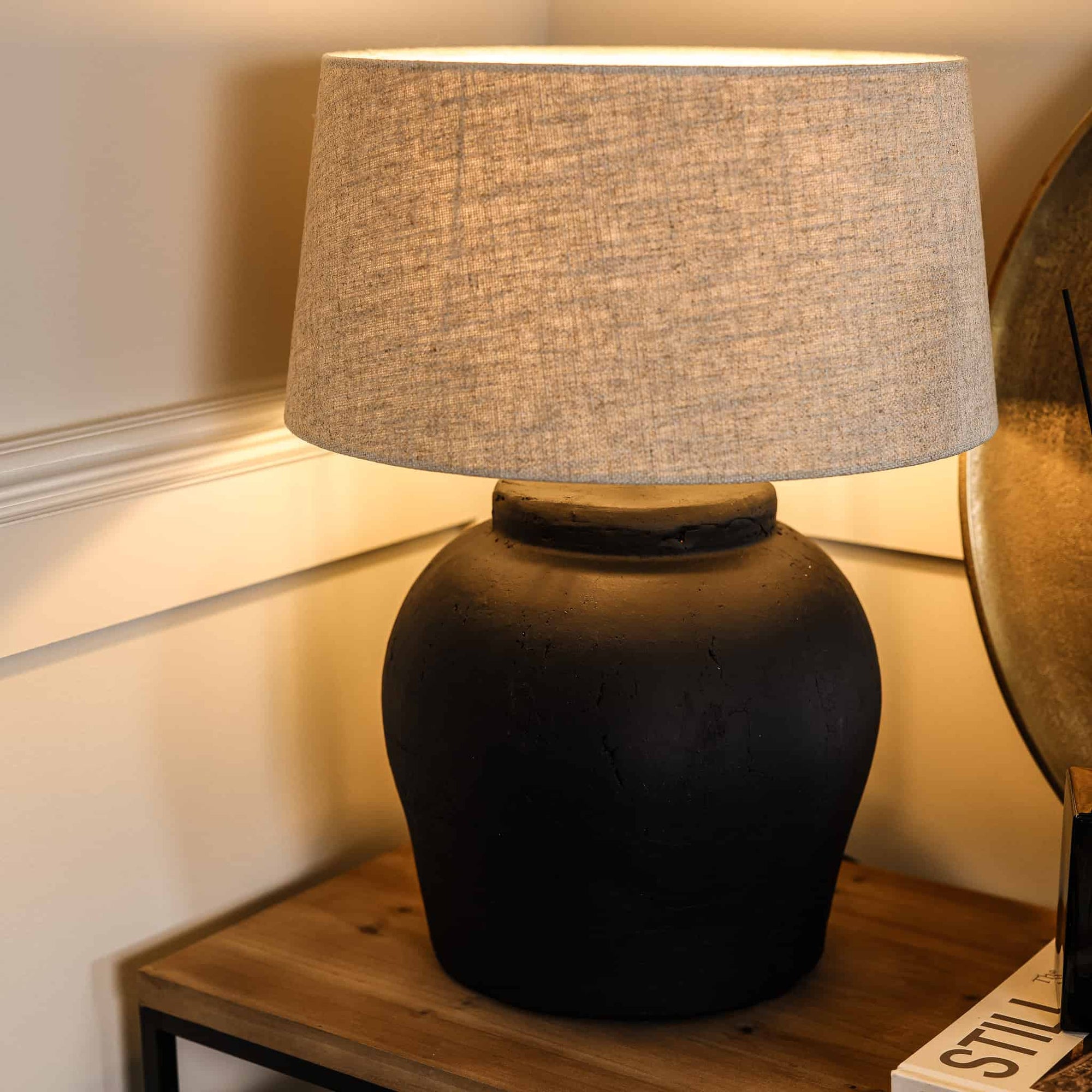 Close up of matte black lamp with neutral shade, switched on on wooden console.