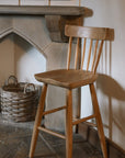 Farmhouse wooden bar stool against stone fire place on a flagged floor.