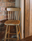 Wooden farmhouse bar stool with back against reclaimed brick wall.