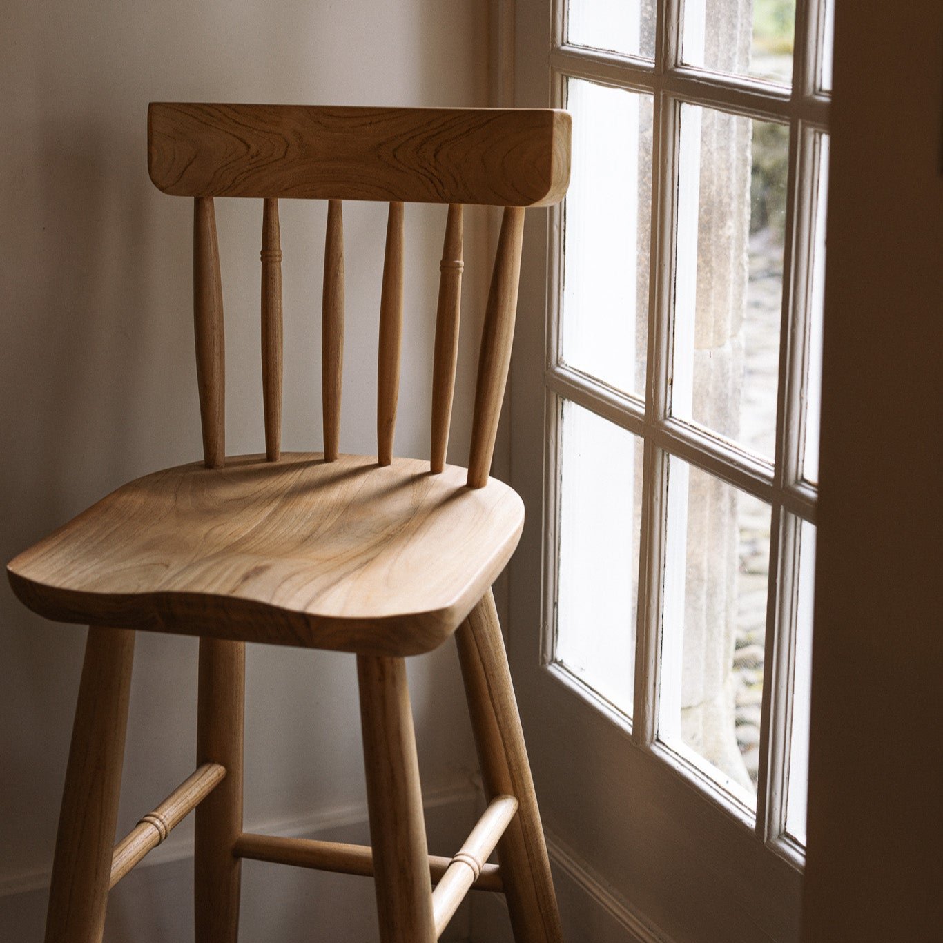 Farmhouse wooden bar stool against window.