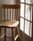 Farmhouse wooden bar stool against window.