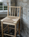 Farmhouse Rattan Bar Stool against an exposed stone wall and patterned floor.
