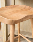 Close up of curved seat on backless wooden bar stool.