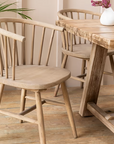 2 vintage inspired wooden carver chair with curved back and spindles, at a wooden dining table with vase on top.