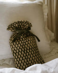 Forest green and natural hot water bottle with green bow tie closure, on white bedspread.