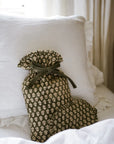 Forest green and natural hot water bottle with green bow tie closure with matching eye mask, on white bedspread.