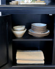 Close up of open cupboard filled with kitchen crockery on black shelving unit.