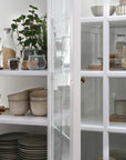 Close up of glass doors on large white armoire cabinet, filled with kitchen accessories.