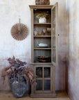 Natural wood display cabinet with glass door open, with dinnerware and glasses on shelves.