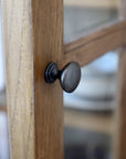 Close up of door knob on natural wood display cabinet.