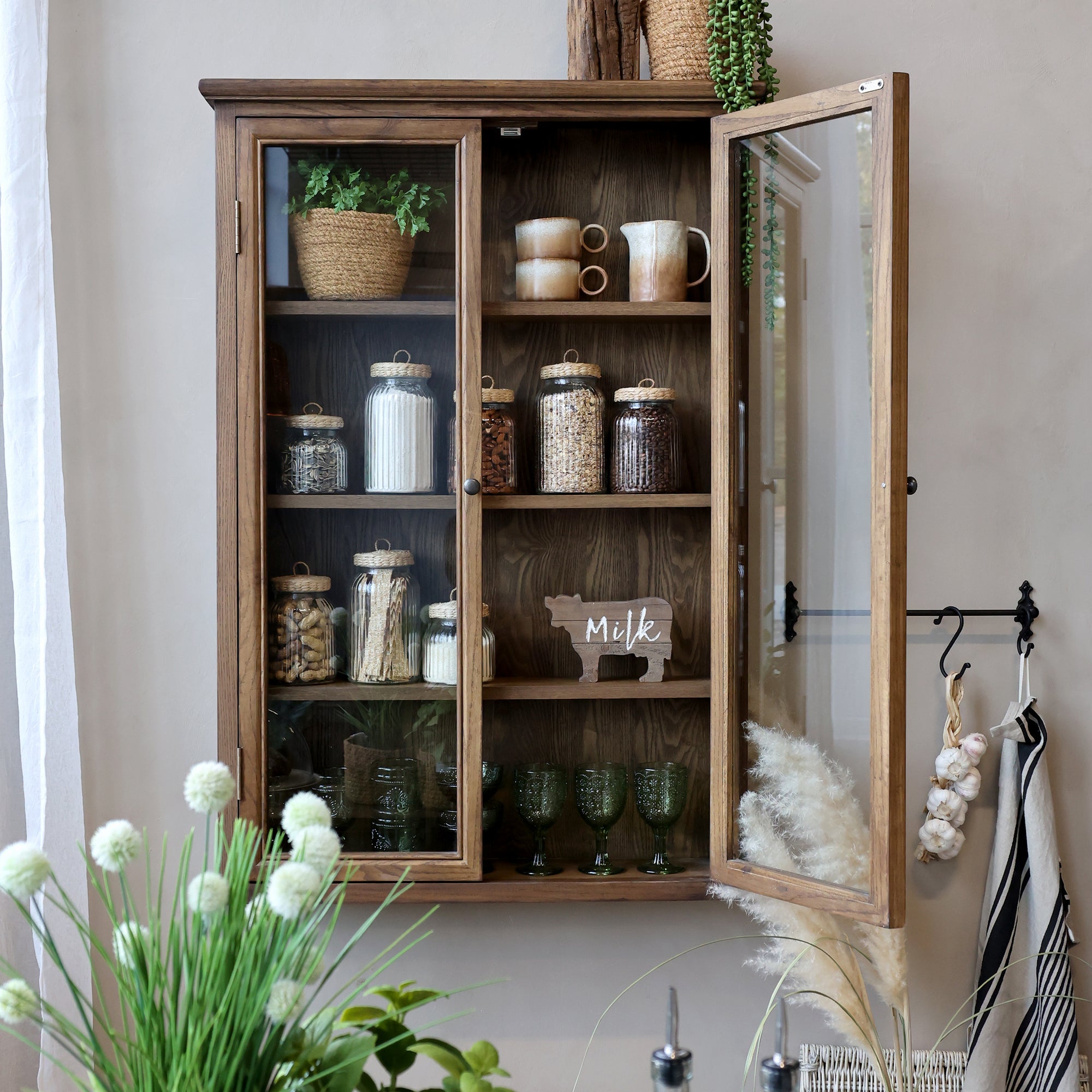Natural wooden wall cabinet with glass doors and pantry items on shelves.
