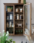 Natural wooden wall cabinet with glass doors and pantry items on shelves.