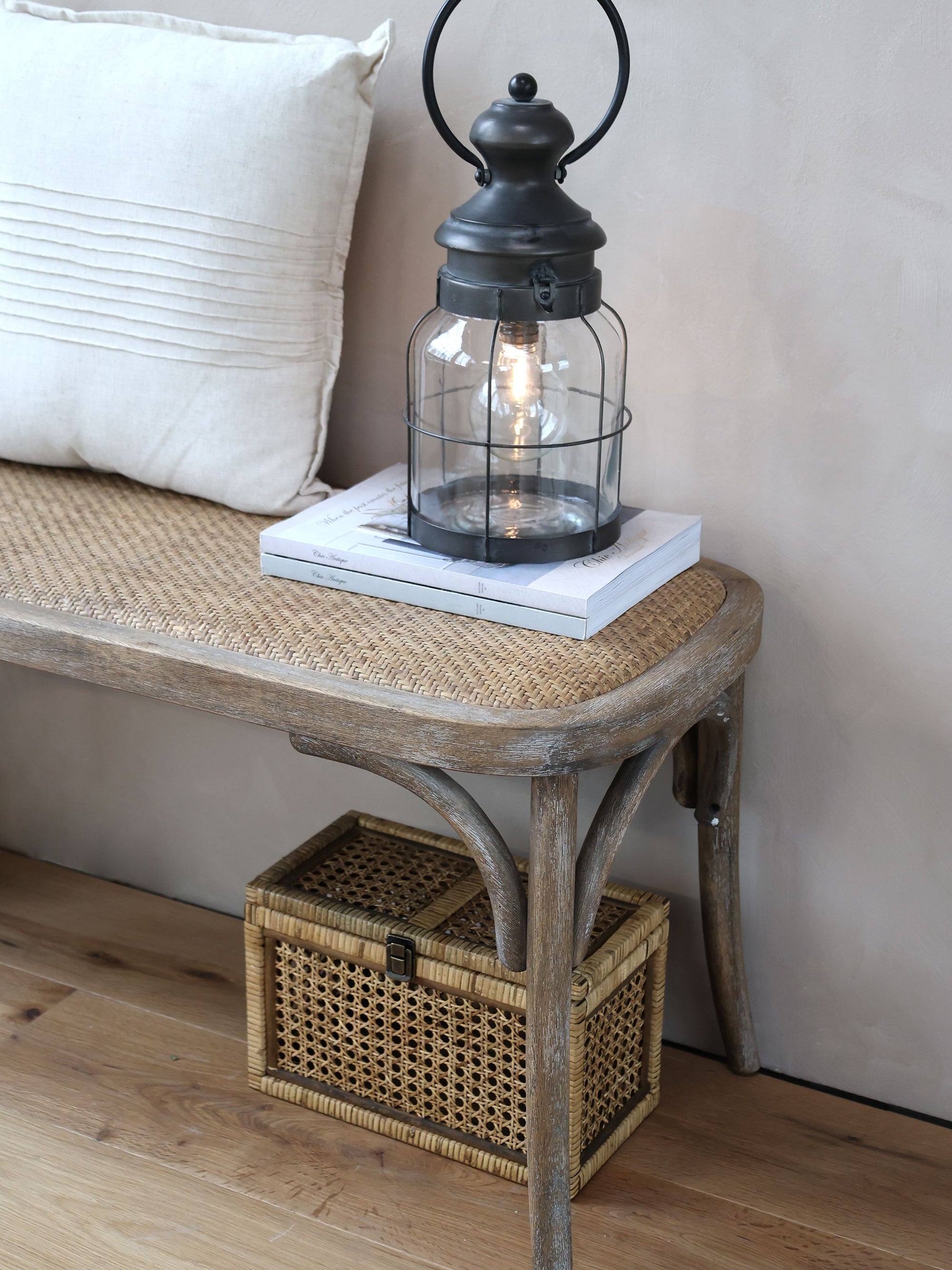 Detailed shot of aRattan Dining Bench with book, cushion and small lantern.