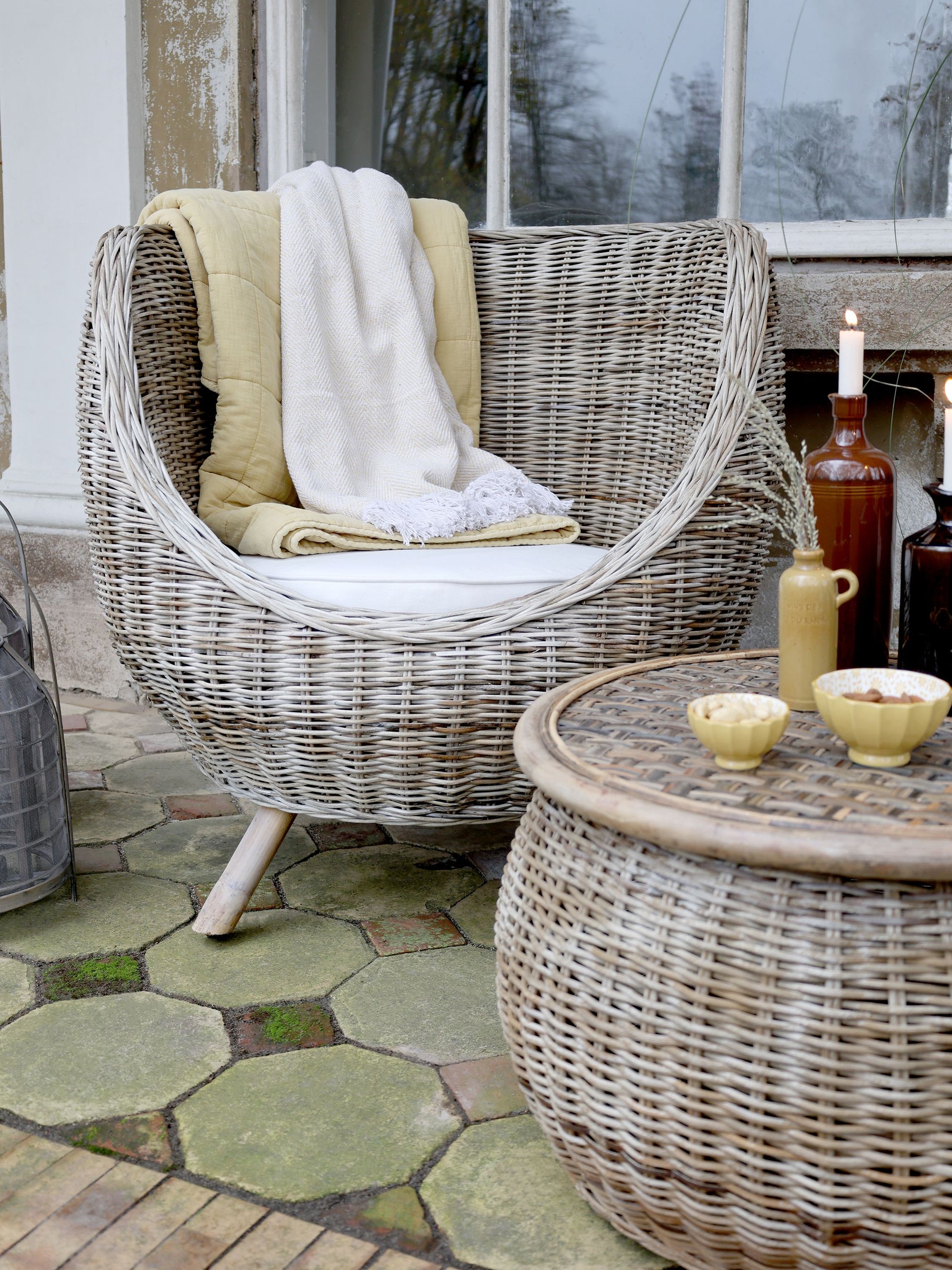 Rattan outdoor armchair with yellow and cream blanket next to rattan table.