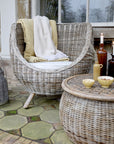 Rattan outdoor armchair with yellow and cream blanket next to rattan table.