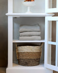 White display cabinet with glass doors open, and towels folded on shelf with other accessories.