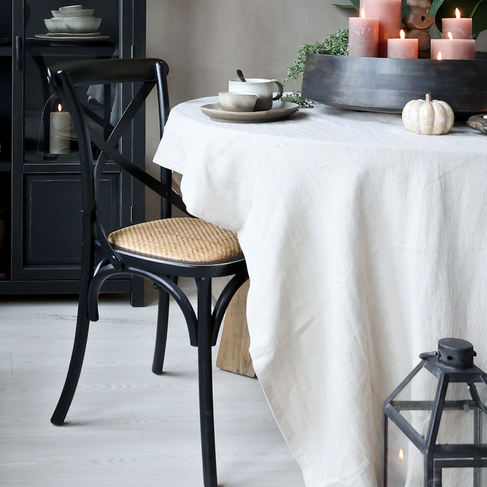 Black wooden dining chair with natural wicker seat at a dining table with table cloth and candles on.