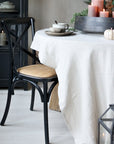 Black wooden dining chair with natural wicker seat at a dining table with table cloth and candles on.
