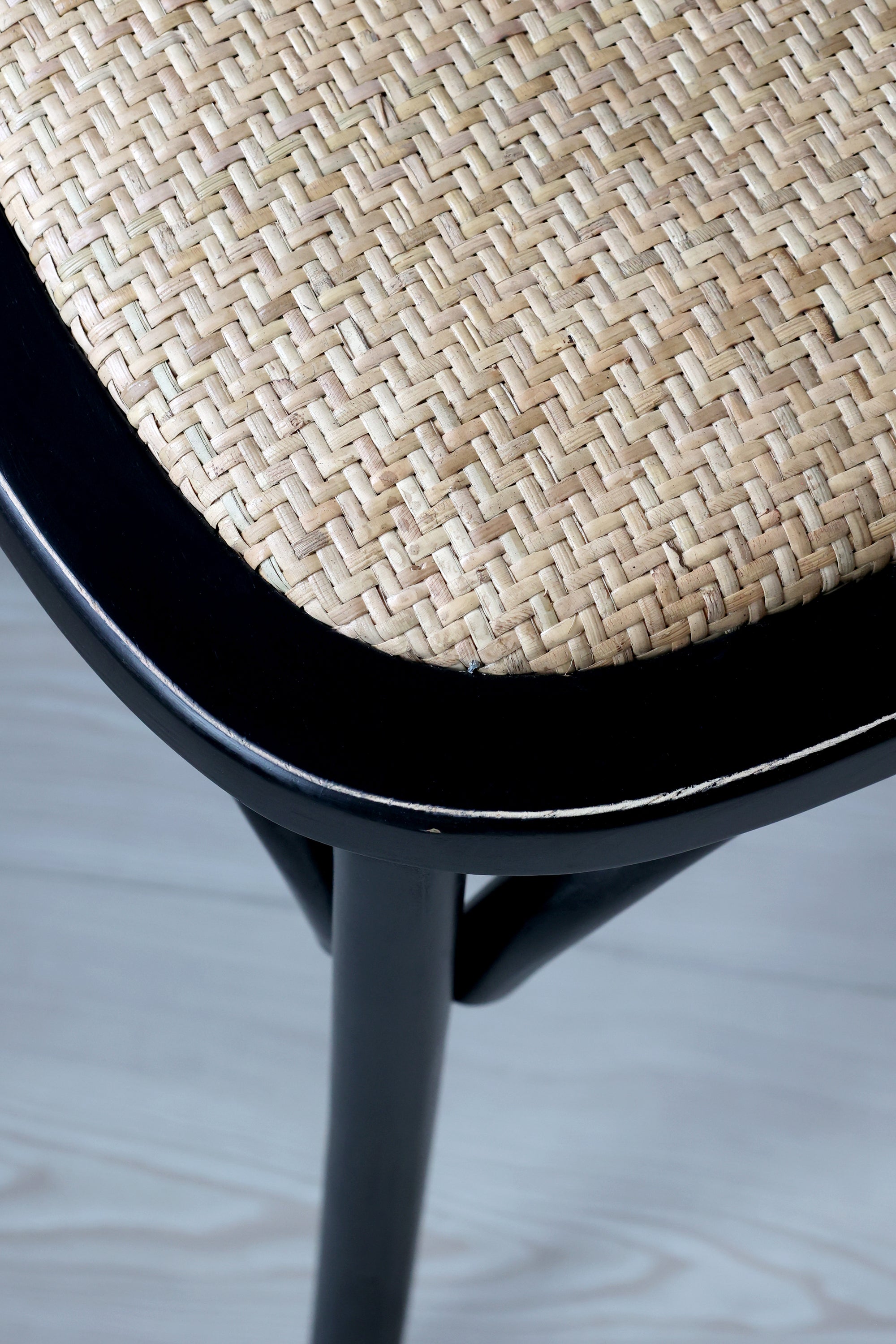 Close up of wicker seat on black wooden dining chair.