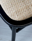 Close up of wicker seat on black wooden dining chair.