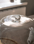 Glass cake dome cloche on wooden table with gingham tea towel.