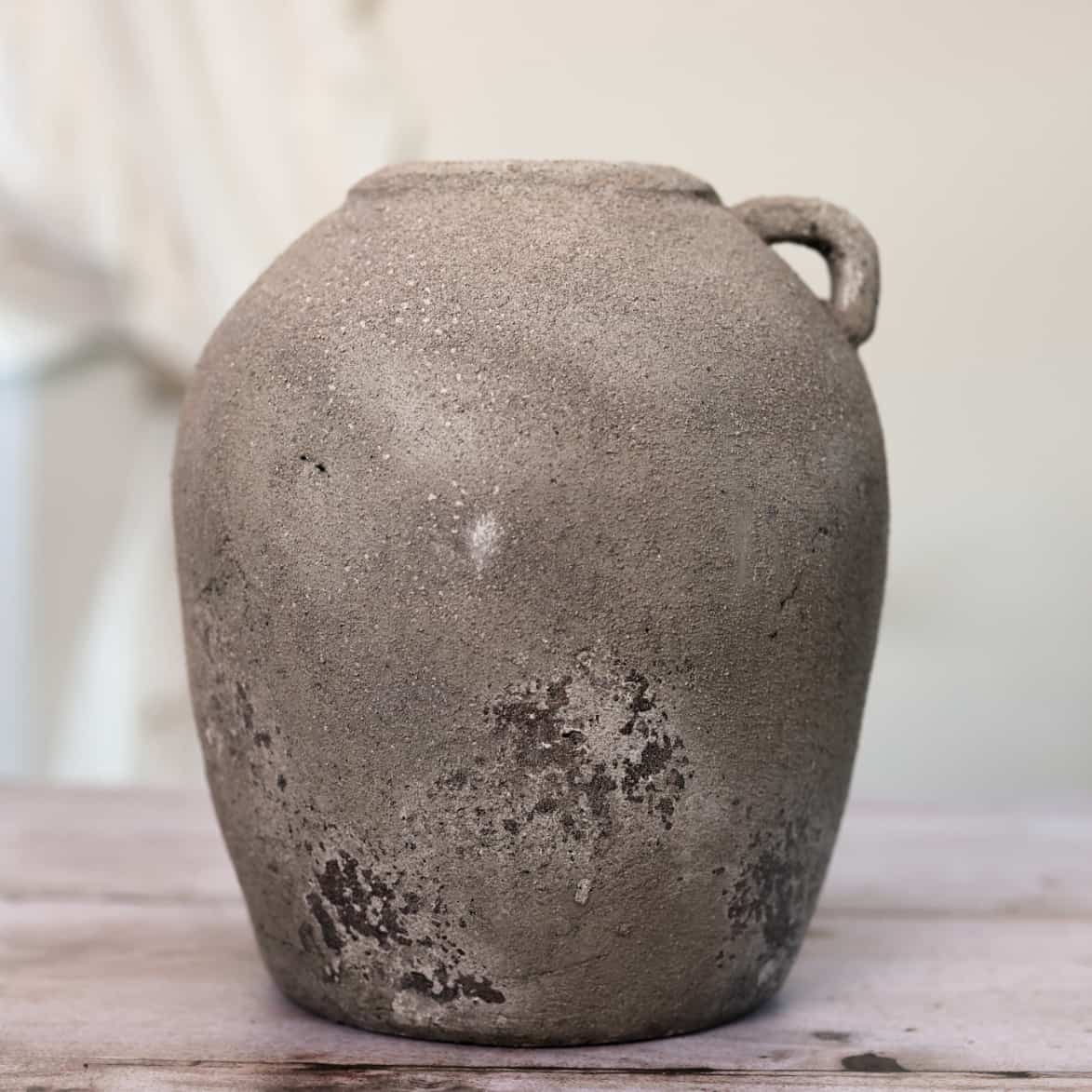 Distressed grey vase with small handle at the top on wooden table.