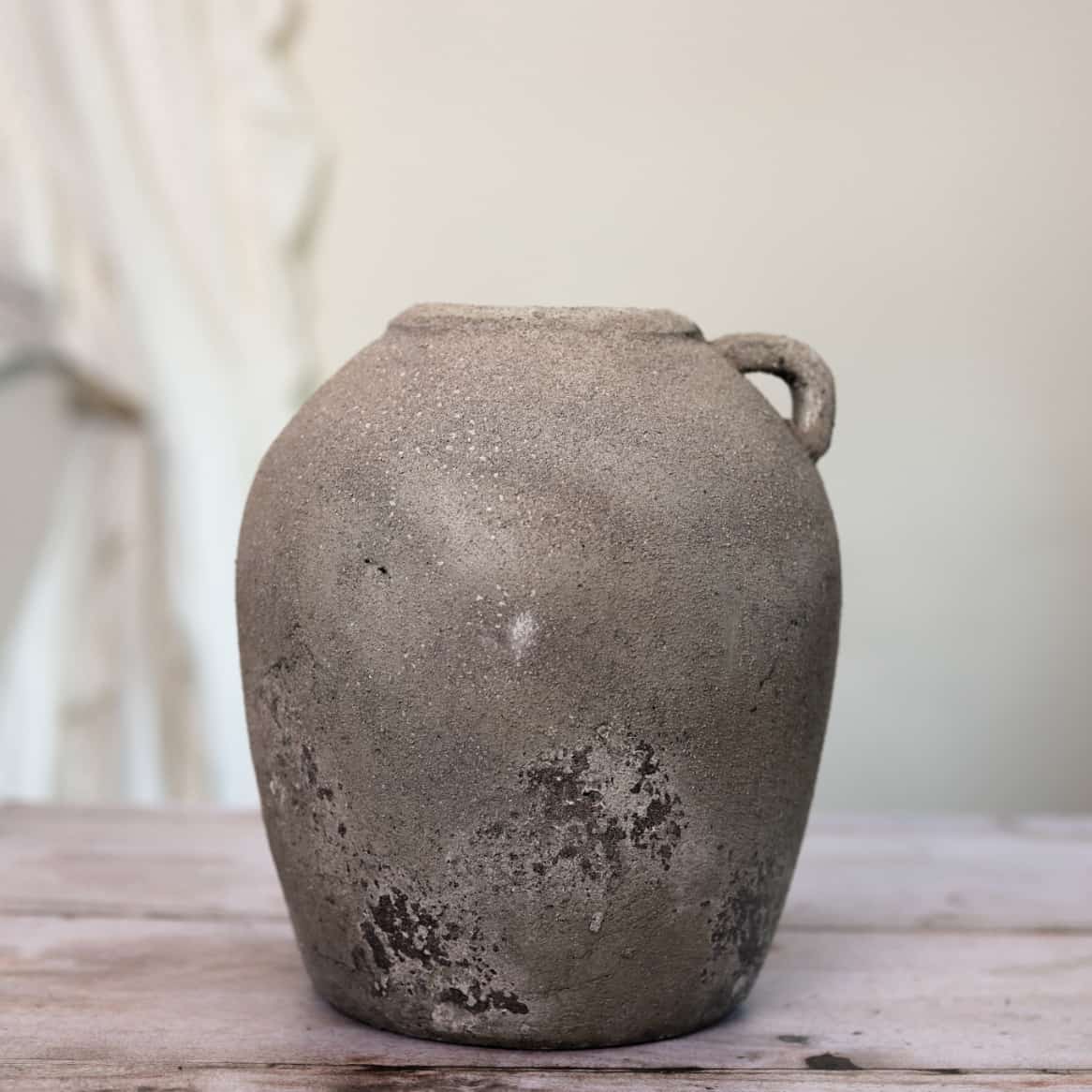 Distressed grey vase with small handle at the top on wooden surface.