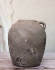 Distressed grey vase with small handle at the top on wooden surface.