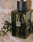 Green florist Sences reed diffuser on stone windowsill with flowers.