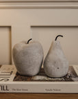 Cement grey washed apple and pear ornaments on white decorative book on wooden console.