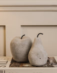 Cement grey washed apple and pear ornaments layered on white decorative book on wooden console.