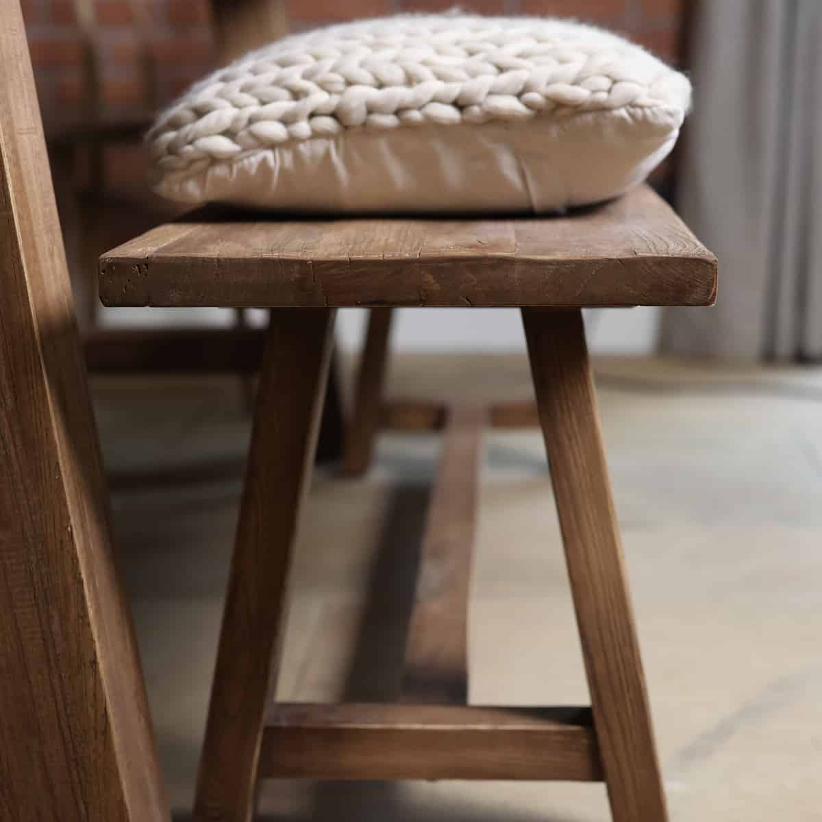 Oak bench side view with cream cushion on top.