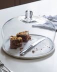 Marble and class cake dome with slice of cake and knife inside.