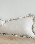 Close up of sand coloured bolster cushion with ruffled edge on wooden surface.