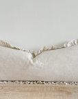 Sand coloured bolster cushion with ruffled edge on wooden surface.
