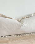 Sand coloured bolster cushion with ruffled edge on wooden surface.